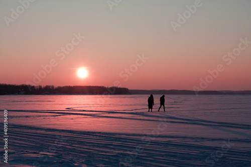 Horizontal dramatic landscape photography of the scene of the parting of a guy and a girl with their silhouettes agains pink cold sunset over horizon