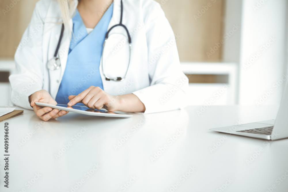 Unknown woman-doctor standing in clinic and using tablet pc, close-up. Data and best service in medicine and healthcare Unknown woman-doctor standing in clinic and using tablet pc, close-up. Data and best service in medicine and healthcare