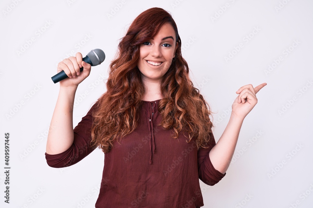 Young beautiful woman singing song using microphone smiling happy pointing with hand and finger to the side Young beautiful woman singing song using microphone smiling happy pointing with hand and finger to the side