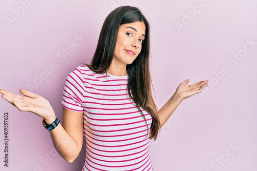 Young brunette woman wearing casual clothes over pink background clueless and confused expression with arms and hands raised. doubt concept.