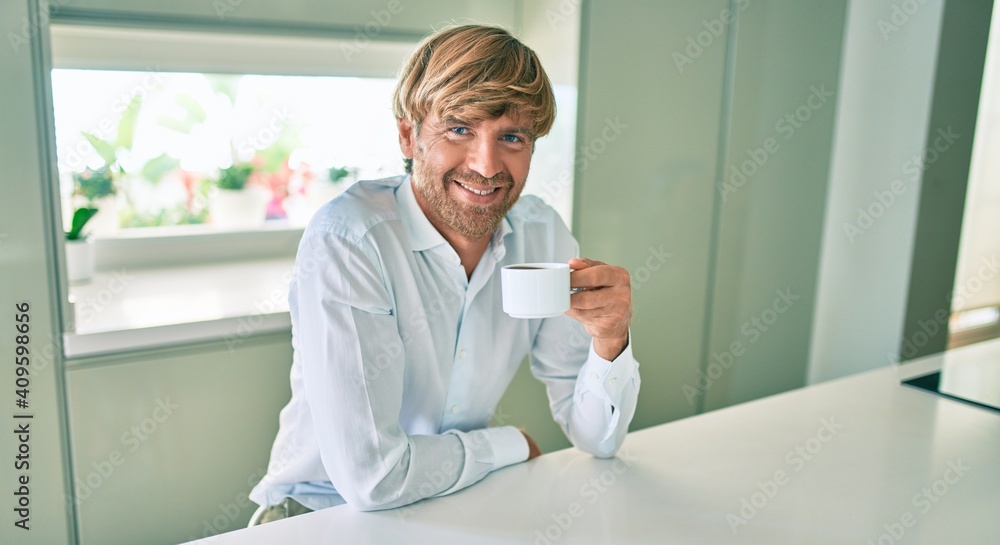 Fototapeta premium Young irish man smiling happy drinking cup of coffee sitting on the table at home.