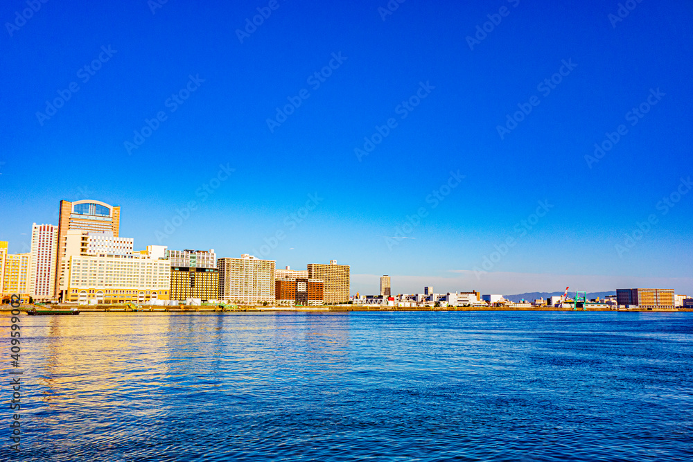 青空を背景に対岸沿いに建つホテルやビル等の建物見た静かな朝の海の風景