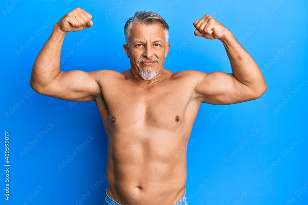 Middle age grey-haired man standing shirtless doing fitness gesture relaxed with serious expression on face. simple and natural looking at the camera.