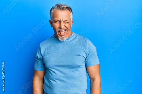 Middle age grey-haired man wearing casual clothes winking looking at the camera with sexy expression, cheerful and happy face.