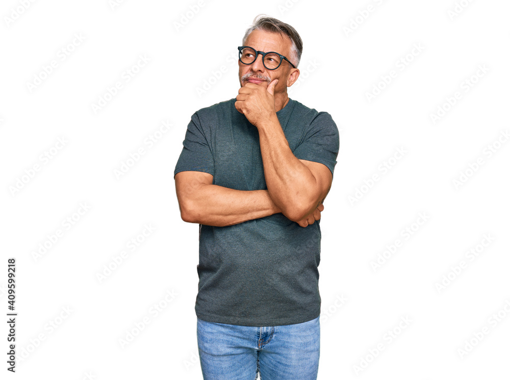 Fototapeta premium Middle age grey-haired man wearing casual clothes and glasses serious face thinking about question with hand on chin, thoughtful about confusing idea