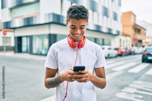 Young latin man smiling happy using smartphone and headphones at the city.