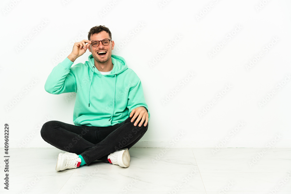 Young handsome caucasian man sitting on the floor with glasses and surprised Young handsome caucasian man sitting on the floor with glasses and surprised