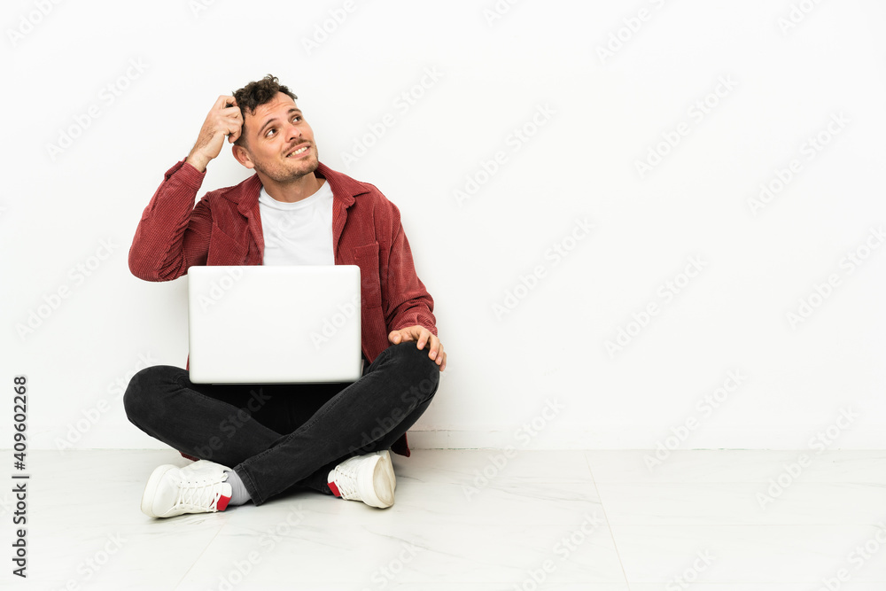 Young handsome caucasian man sit-in on the floor with laptop having doubts and with confuse face expression Young handsome caucasian man sit-in on the floor with laptop having doubts and with confuse face expression