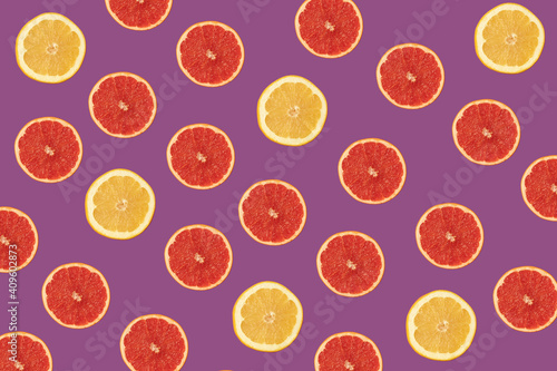 Pattern made of red and yellow grapefruit on vivid purple background. Fresh organic food in vibrant colors.