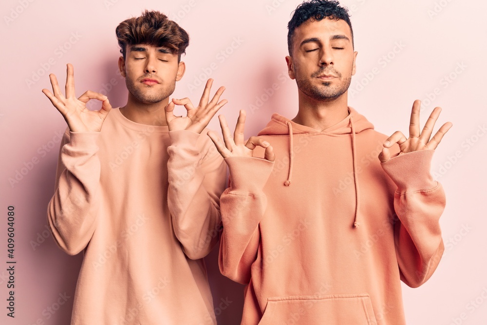 Young gay couple wearing casual clothes relaxed and smiling with eyes closed doing meditation gesture with fingers. yoga concept. Young gay couple wearing casual clothes relaxed and smiling with eyes closed doing meditation gesture with fingers. yoga concept.