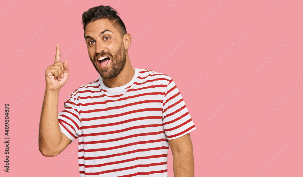Handsome man with beard wearing striped tshirt pointing finger up with successful idea. exited and happy. number one. Handsome man with beard wearing striped tshirt pointing finger up with successful idea. exited and happy. number one.