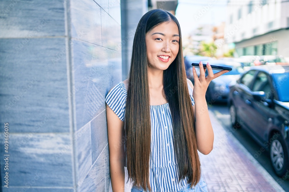 Fototapeta premium Young chinese woman smiling happy talking on the smartphone at street of city.