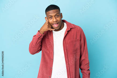 Young latin man isolated on blue background making phone gesture. Call me back sign