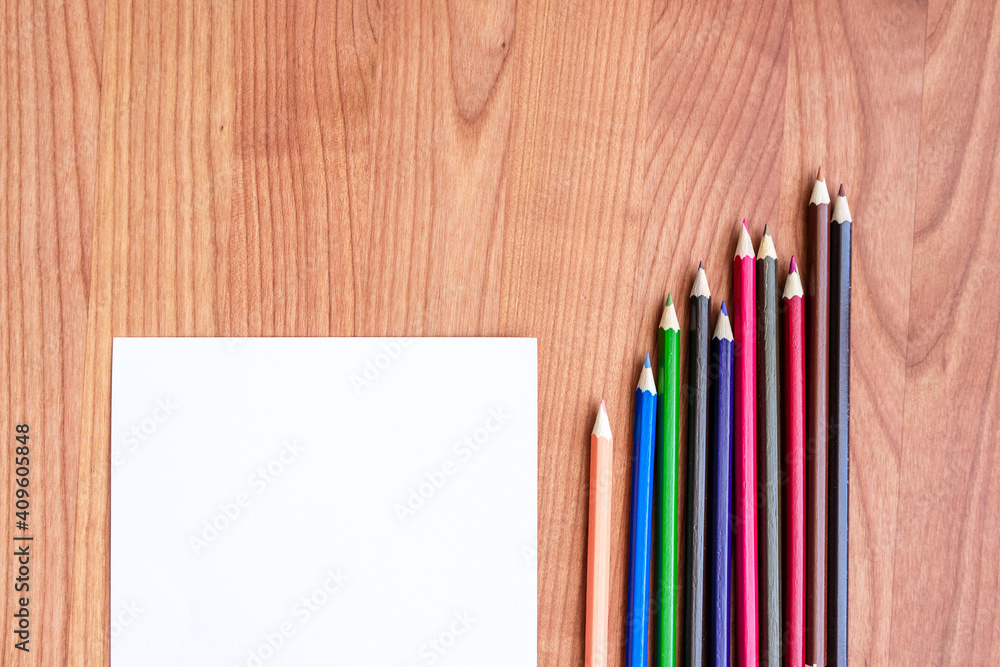 Obraz premium Ein unbeschriebener Notizzettel und Buntsifte auf einem braunen Holz Tisch. Flat lay, Kreativität, Schule.