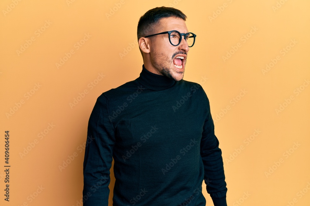 Handsome man with tattoos wearing turtleneck sweater and glasses angry and mad screaming frustrated and furious, shouting with anger. rage and aggressive concept. Handsome man with tattoos wearing turtleneck sweater and glasses angry and mad screaming frustrated and furious, shouting with anger. rage and aggressive concept.