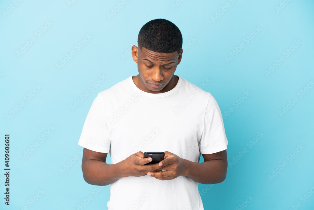 Young latin man isolated on blue background using mobile phone Young latin man isolated on blue background using mobile phone