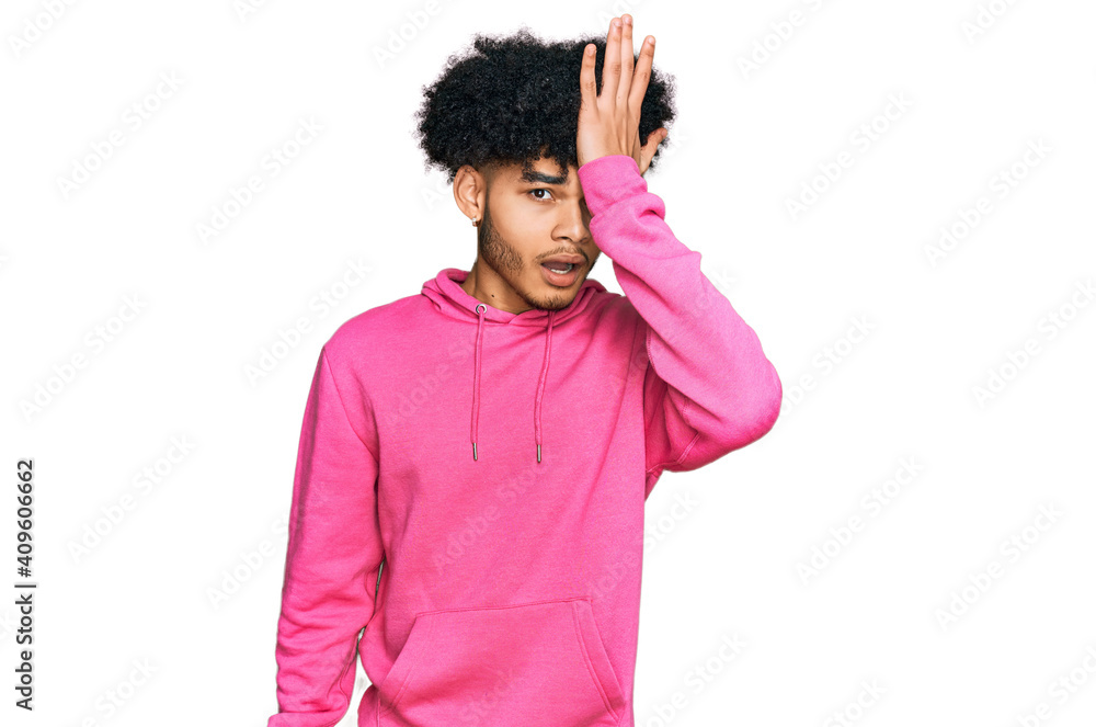 Young african american man with afro hair wearing casual pink sweatshirt surprised with hand on head for mistake, remember error. forgot, bad memory concept. Young african american man with afro hair wearing casual pink sweatshirt surprised with hand on head for mistake, remember error. forgot, bad memory concept.