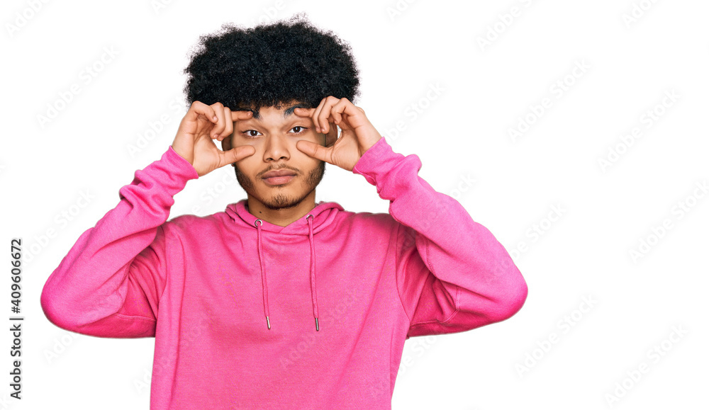 Young african american man with afro hair wearing casual pink sweatshirt trying to open eyes with fingers, sleepy and tired for morning fatigue Young african american man with afro hair wearing casual pink sweatshirt trying to open eyes with fingers, sleepy and tired for morning fatigue