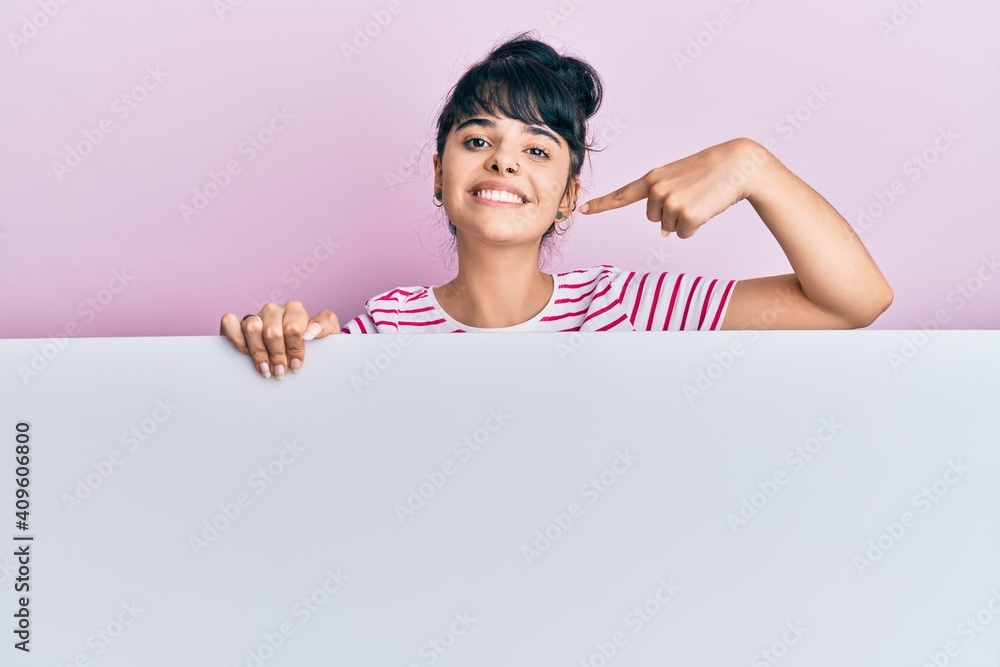 Young hispanic girl holding blank empty banner pointing finger to one self smiling happy and proud Young hispanic girl holding blank empty banner pointing finger to one self smiling happy and proud