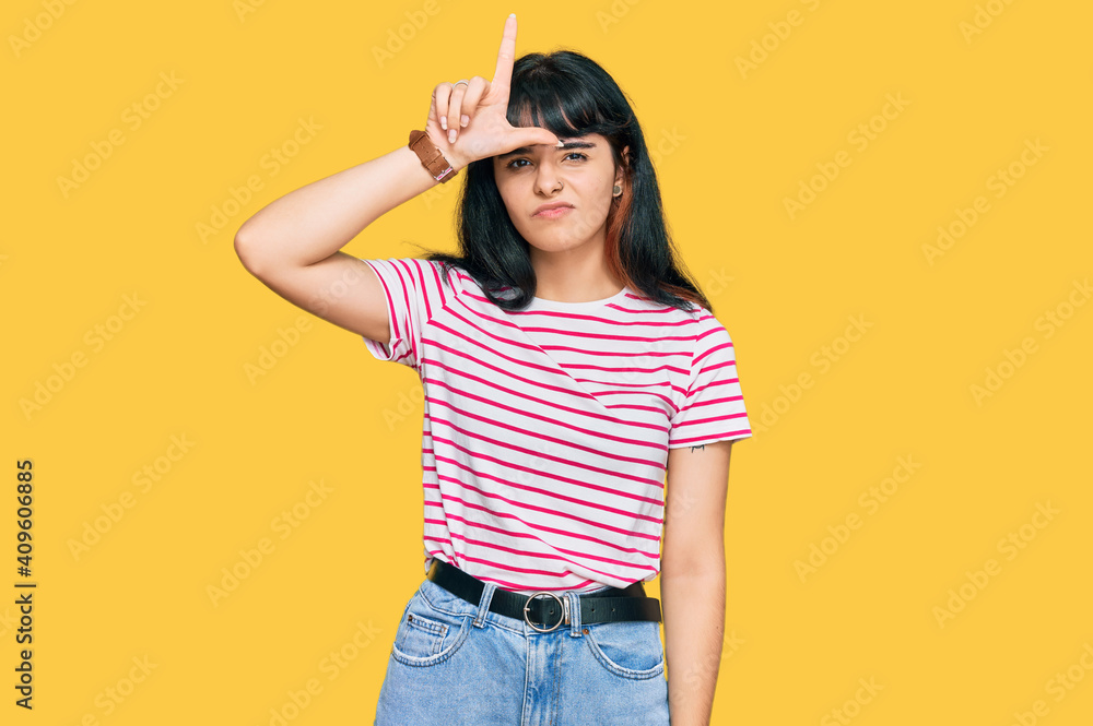 Young hispanic girl wearing casual clothes making fun of people with fingers on forehead doing loser gesture mocking and insulting. Young hispanic girl wearing casual clothes making fun of people with fingers on forehead doing loser gesture mocking and insulting.