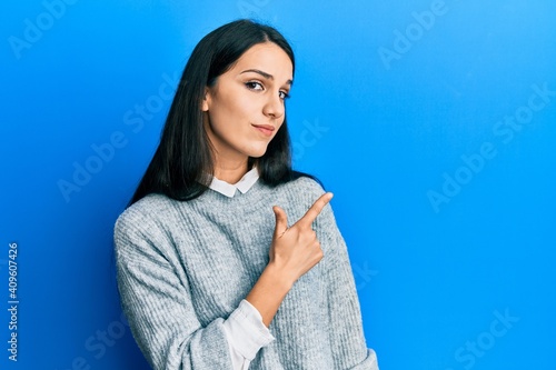 Young hispanic woman wearing casual clothes pointing with hand finger to the side showing advertisement, serious and calm face
