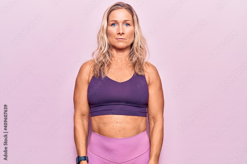 Middle age caucasian blonde woman wearing sportswear over pink background with serious expression on face. simple and natural looking at the camera. Middle age caucasian blonde woman wearing sportswear over pink background with serious expression on face. simple and natural looking at the camera.