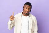 Telemarketer latin man working with a headset isolated on purple background showing and lifting a finger in sign of the best