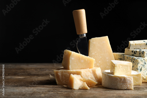 Different sorts of cheese and knife on wooden table against black background. Space for text