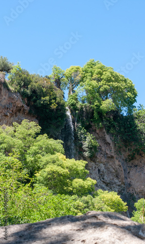 small waterfall among green trees blue sky on background