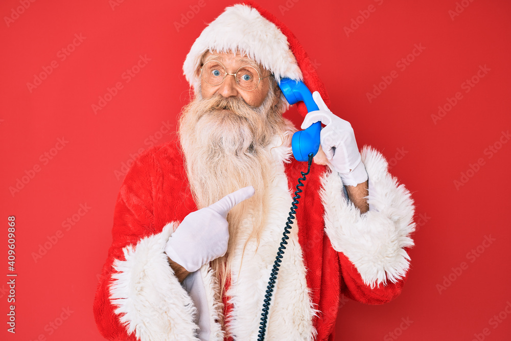 Old senior man wearing santa claus costume using vintage telephone smiling happy pointing with hand and finger Old senior man wearing santa claus costume using vintage telephone smiling happy pointing with hand and finger