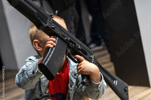 The child holds his finger on the trigger of a machine gun. Demonstration of modern weapons. Close-up. Unrecognizable face