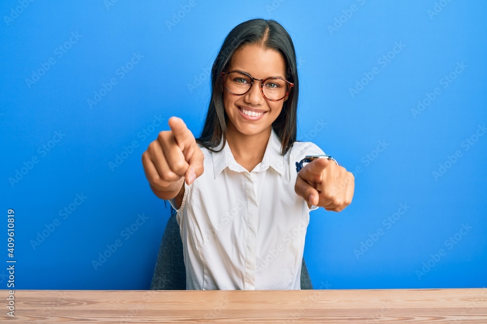 Beautiful hispanic woman wearing casual clothes sitting on the table pointing to you and the camera with fingers, smiling positive and cheerful Beautiful hispanic woman wearing casual clothes sitting on the table pointing to you and the camera with fingers, smiling positive and cheerful