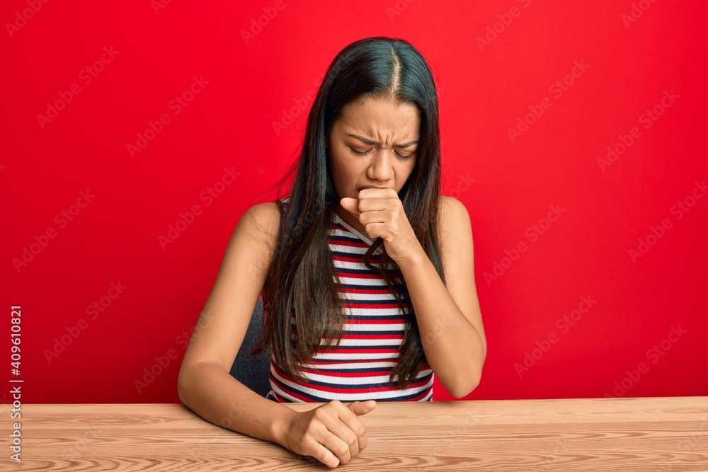 Beautiful hispanic woman wearing casual clothes sitting on the table feeling unwell and coughing as symptom for cold or bronchitis. health care concept. Beautiful hispanic woman wearing casual clothes sitting on the table feeling unwell and coughing as symptom for cold or bronchitis. health care concept.