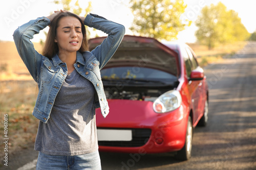 Stressed young woman near broken car outdoors