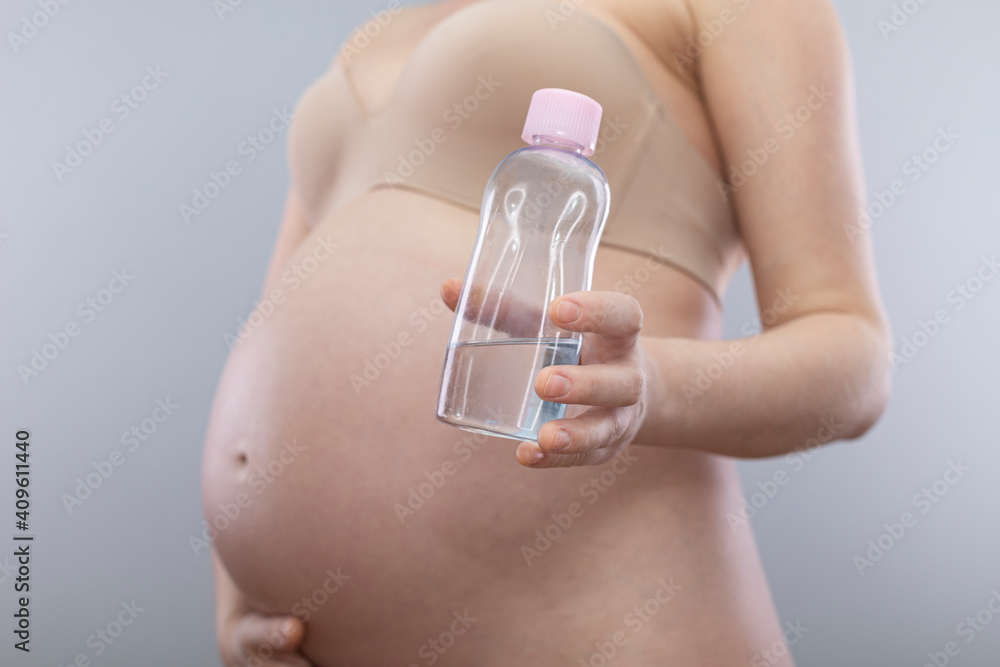 Pregnant woman holds body oil for stretch marks. Pregnant belly isolated on a grey background Pregnant woman holds body oil for stretch marks. Pregnant belly isolated on a grey background