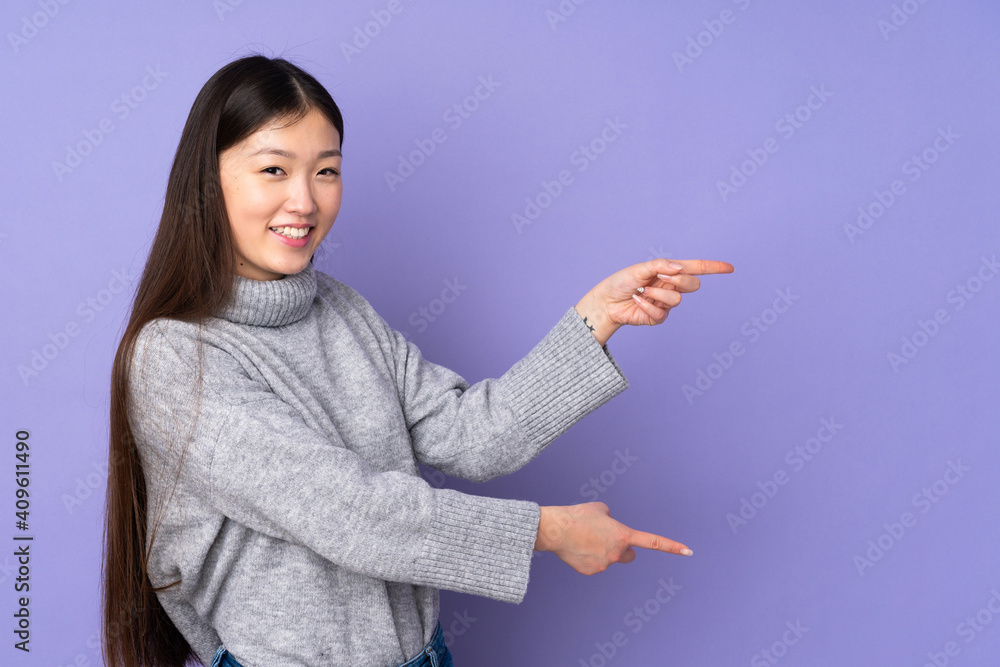 Young asian woman over isolated background pointing finger to the side and presenting a product Young asian woman over isolated background pointing finger to the side and presenting a product