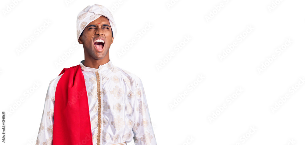 African handsome man wearing tradition sherwani saree clothes angry and mad screaming frustrated and furious, shouting with anger. rage and aggressive concept.