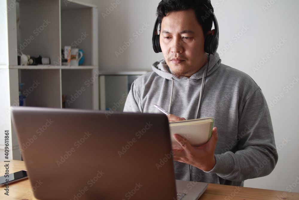 Asian man having video teleconference on his laptop at home, online learning or working from home Asian man having video teleconference on his laptop at home, online learning or working from home
