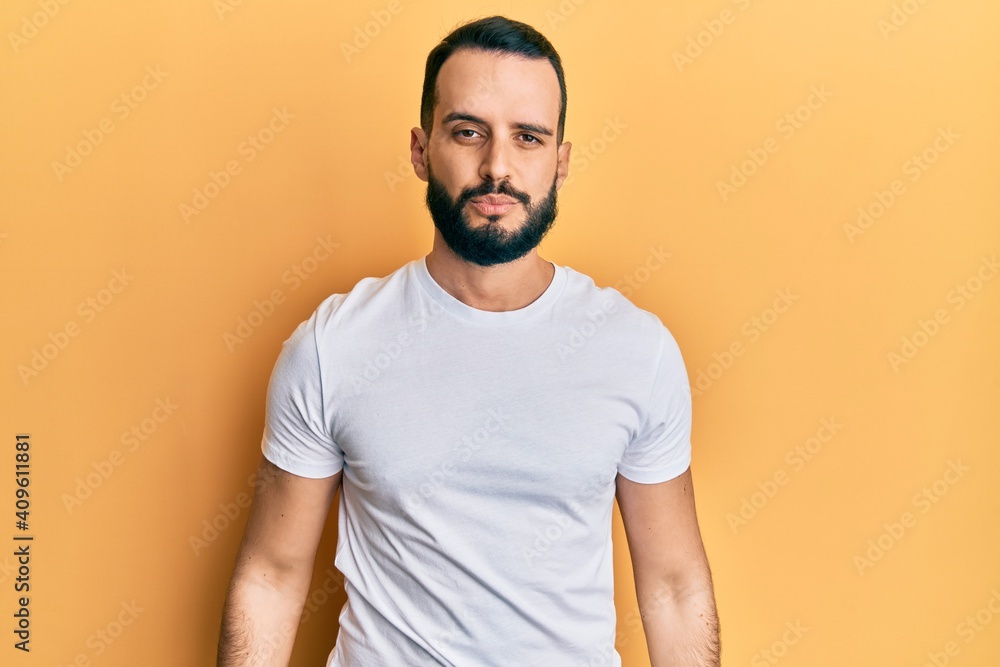 Young man with beard wearing casual white t shirt with serious expression on face. simple and natural looking at the camera. Young man with beard wearing casual white t shirt with serious expression on face. simple and natural looking at the camera.