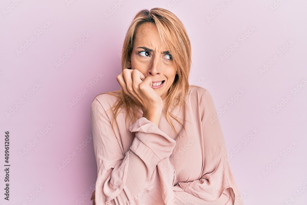 Beautiful blonde woman wearing casual winter sweater looking stressed and nervous with hands on mouth biting nails. anxiety problem. Beautiful blonde woman wearing casual winter sweater looking stressed and nervous with hands on mouth biting nails. anxiety problem.