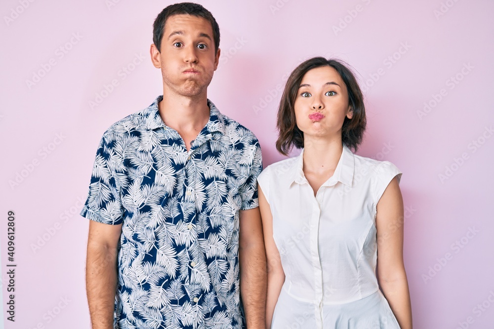 Beautiful couple wearing casual clothes puffing cheeks with funny face. mouth inflated with air, crazy expression. Beautiful couple wearing casual clothes puffing cheeks with funny face. mouth inflated with air, crazy expression.