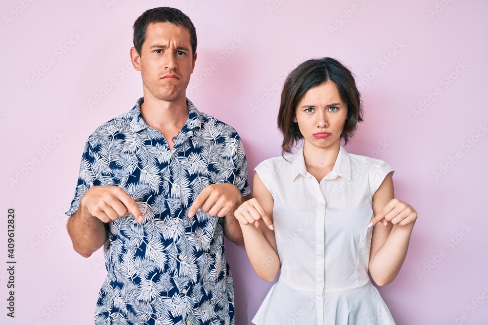 Beautiful couple wearing casual clothes pointing down looking sad and upset, indicating direction with fingers, unhappy and depressed. Beautiful couple wearing casual clothes pointing down looking sad and upset, indicating direction with fingers, unhappy and depressed.