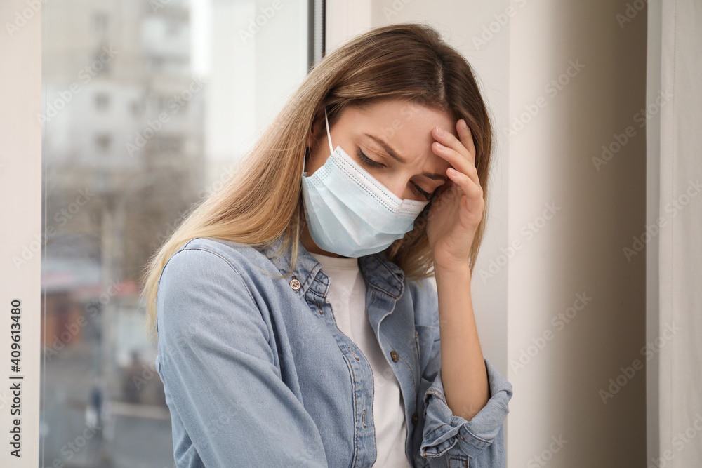 Sad woman in protective mask near window indoors. Staying at home during coronavirus pandemic Sad woman in protective mask near window indoors. Staying at home during coronavirus pandemic