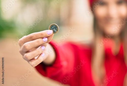 Young hispanic woman wearing wool cap holding 1 euro coin at the city.
