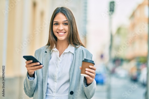 Young latin businesswoman using smartphone and drinking coffee at the city.