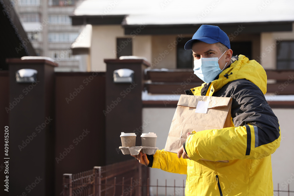 Courier in medical mask holding takeaway food and drinks near house outdoors. Delivery service during quarantine due to Covid-19 outbreak Courier in medical mask holding takeaway food and drinks near house outdoors. Delivery service during quarantine due to Covid-19 outbreak