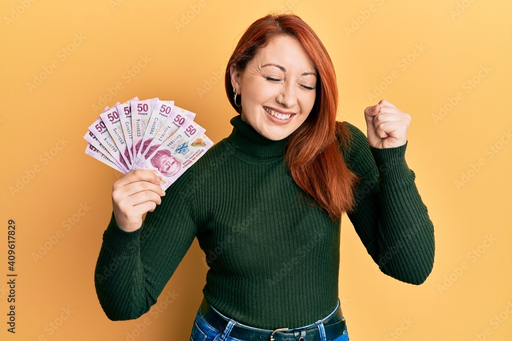 Beautiful redhead woman holding 50 mexican pesos banknotes screaming proud, celebrating victory and success very excited with raised arm Beautiful redhead woman holding 50 mexican pesos banknotes screaming proud, celebrating victory and success very excited with raised arm