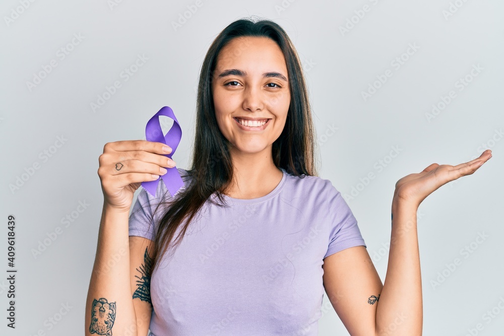 Young hispanic woman holding purple ribbon awareness celebrating victory with happy smile and winner expression with raised hands Young hispanic woman holding purple ribbon awareness celebrating victory with happy smile and winner expression with raised hands