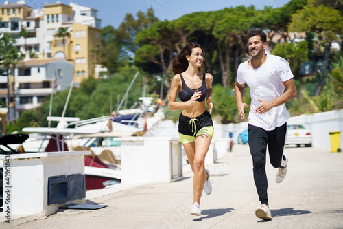 Young couple training together running near the boats in a harbour