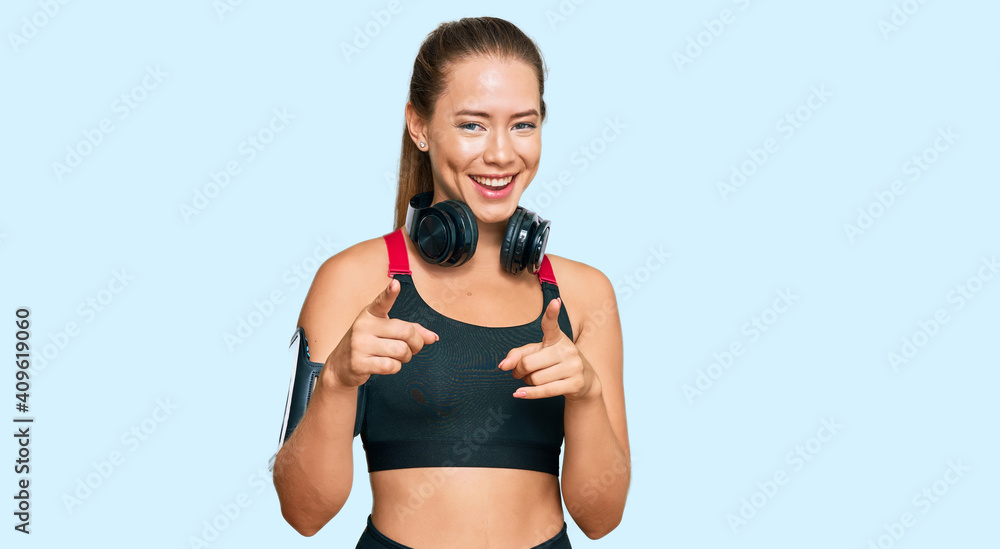 Beautiful blonde woman wearing gym clothes and using headphones pointing fingers to camera with happy and funny face. good energy and vibes. Beautiful blonde woman wearing gym clothes and using headphones pointing fingers to camera with happy and funny face. good energy and vibes.